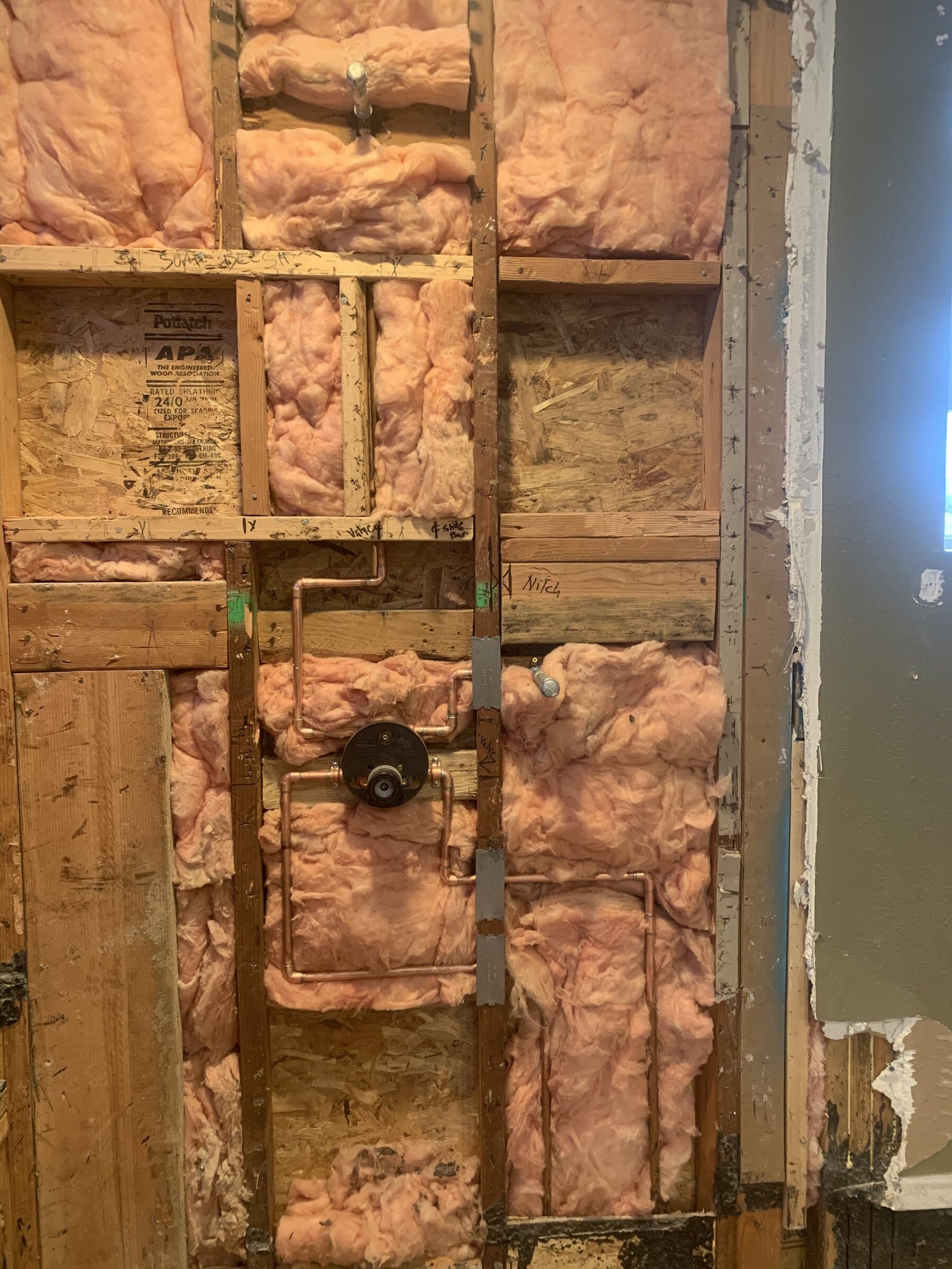 Open stud wall showing a copper shower rough-in with a thermostatic mixing valve body, soldered risers and drop-ear elbows secured to blocking