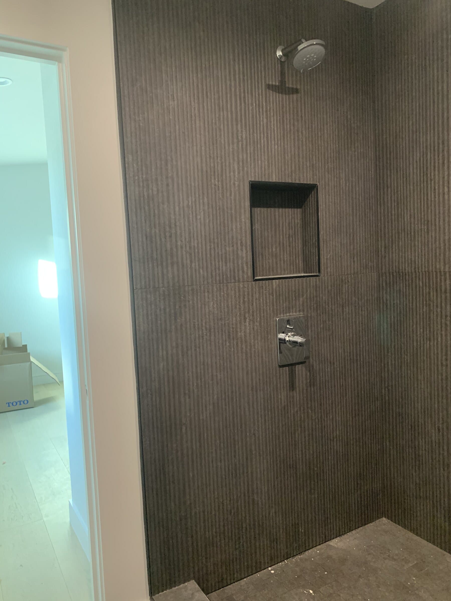 Finished walk-in shower with dark vertical ribbed tile, a recessed niche, a thermostatic control and a ceiling-mounted rain head