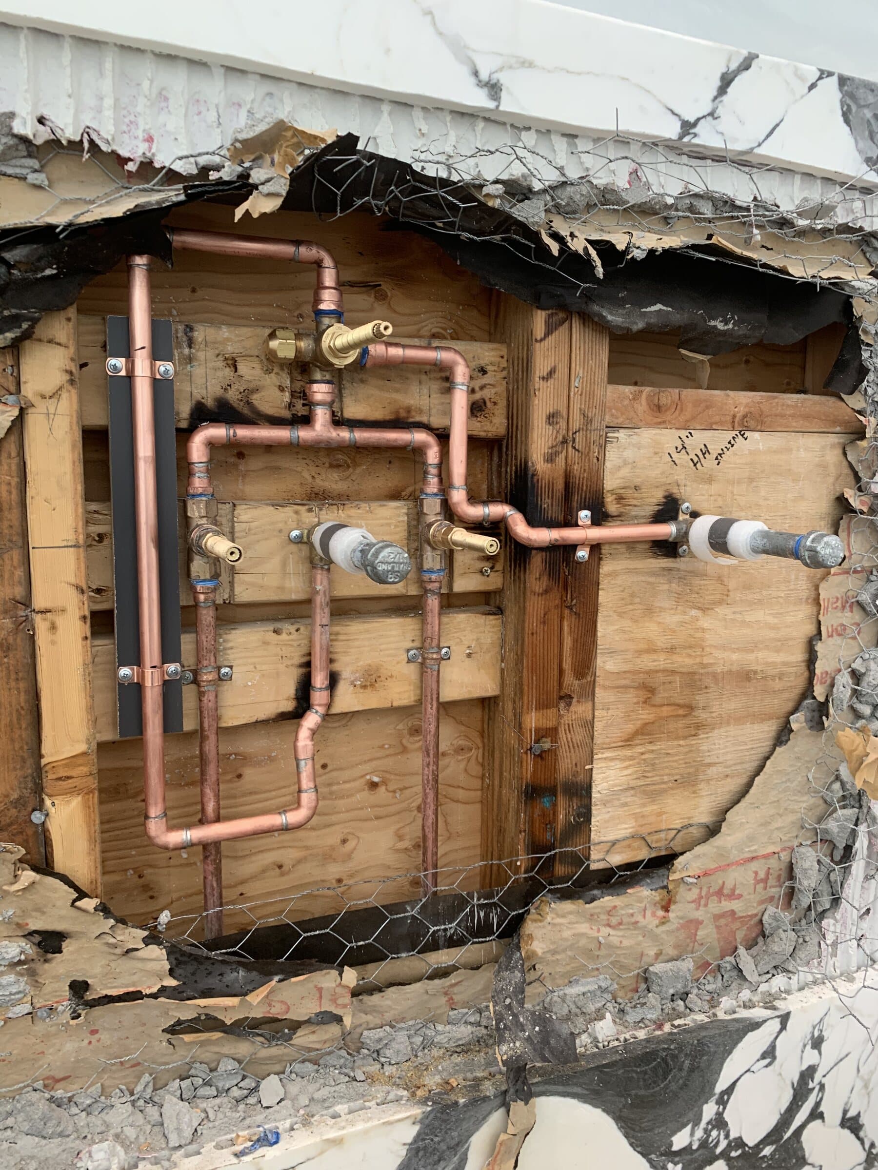 Opened plaster and lath wall exposing newly run copper water lines with soldered joints and shutoff valves during a repipe