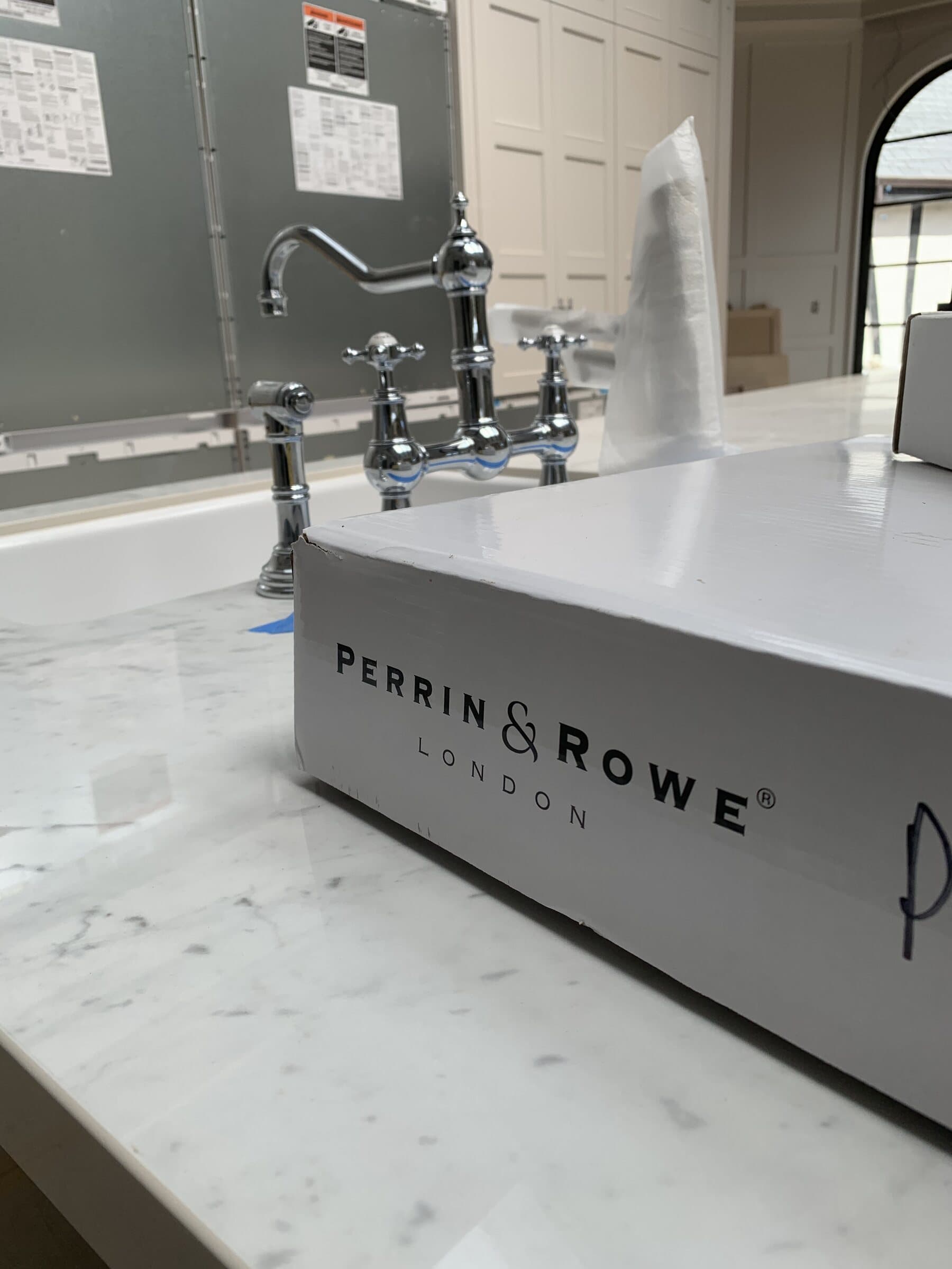 Perrin & Rowe polished chrome bridge faucet with cross handles and a side spray, set on a Carrara marble vanity top in a bathroom under construction