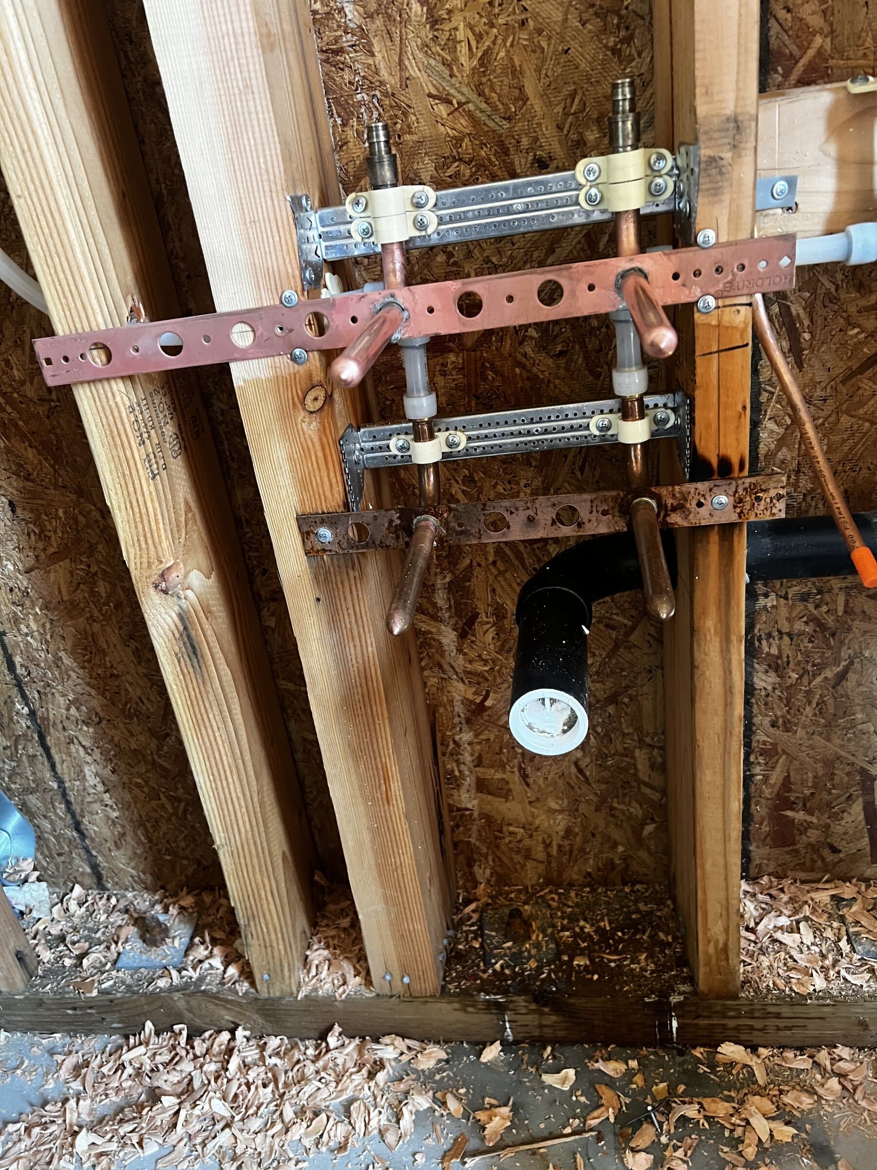 Copper and ABS piping secured to a strut channel between wall studs in an open framed wall during a remodel rough-in