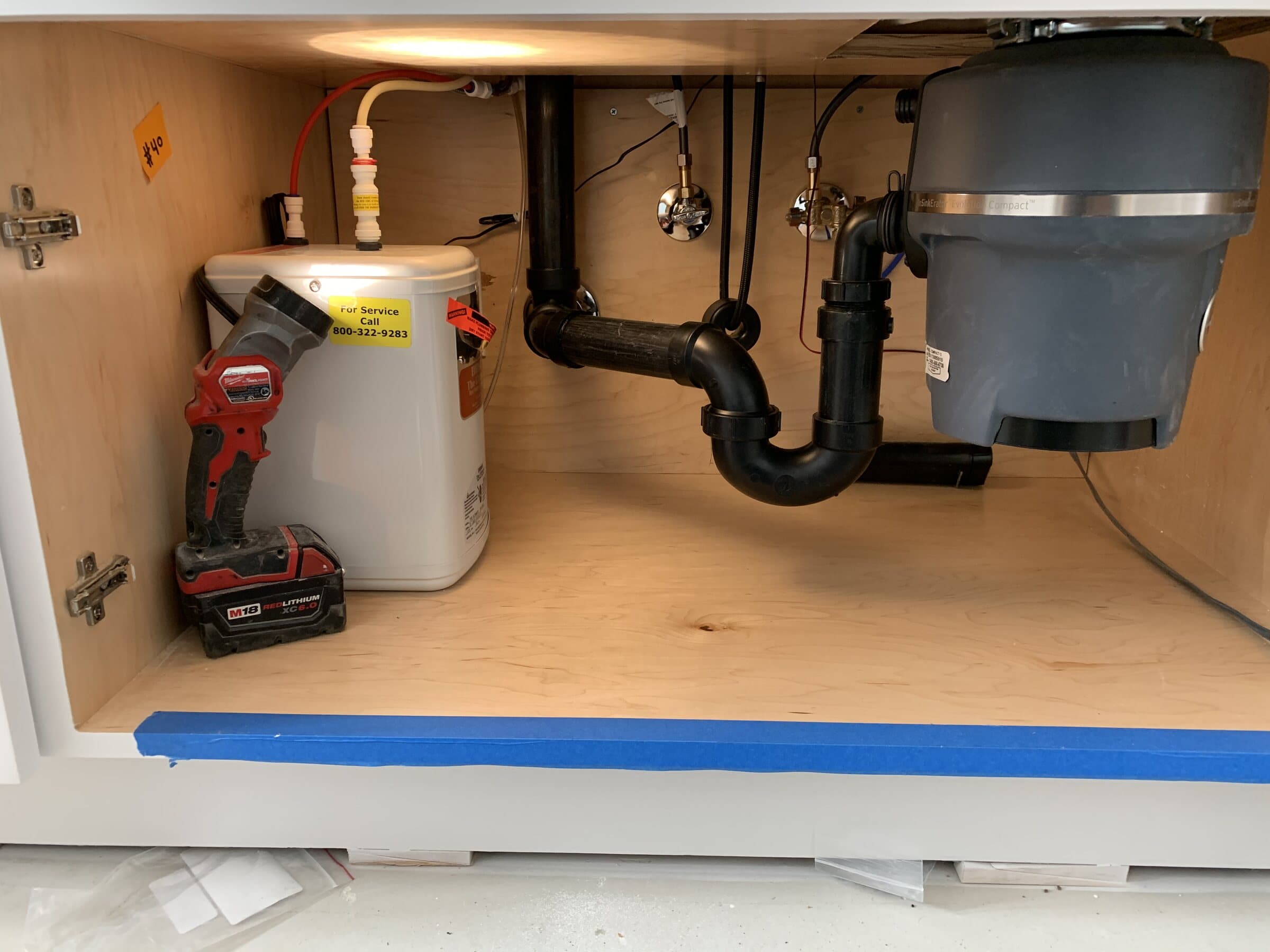Under-sink cabinet with an instant hot water tank, garbage disposal, ABS P-trap and waste arm, with the cabinet edge masked off with painter's tape