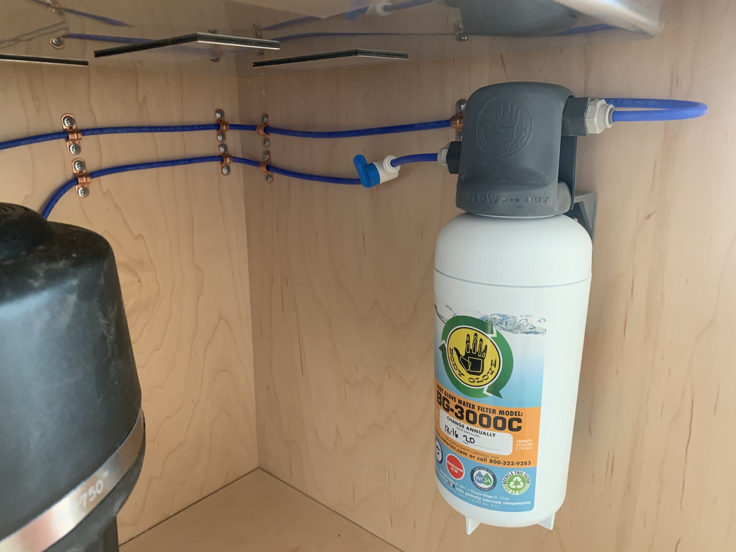 Under-sink water filtration system with a cartridge housing, blue PEX supply lines and shutoff valves inside a kitchen cabinet