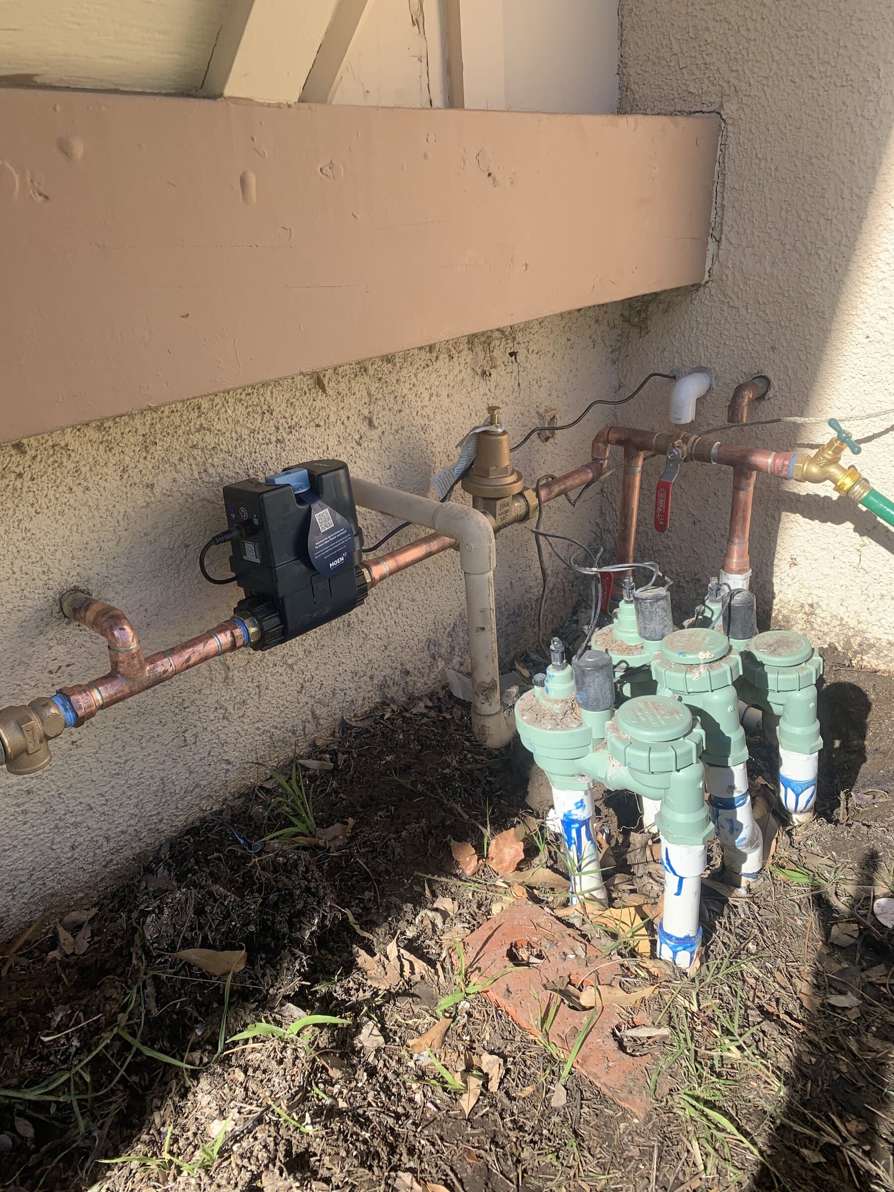 Exterior water main with a pressure regulator, brass shutoff valves and copper piping mounted against a wall above irrigation valves