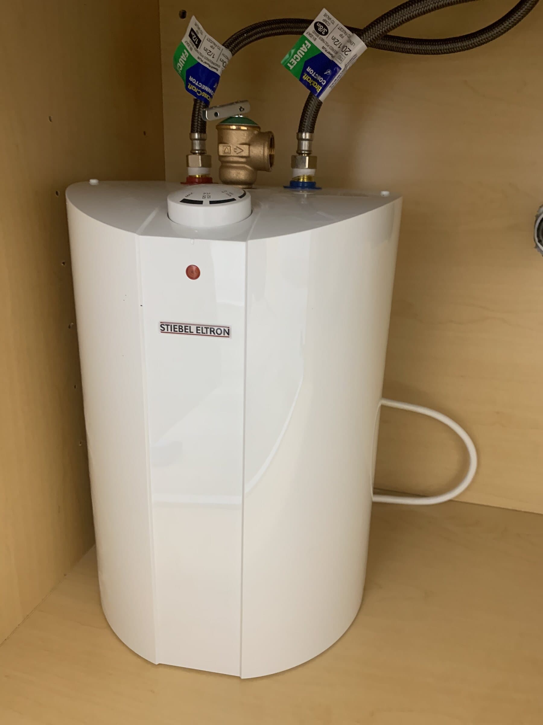 Point-of-use mini-tank electric water heater mounted in a cabinet with a bronze temperature and pressure relief valve and braided stainless supply connectors